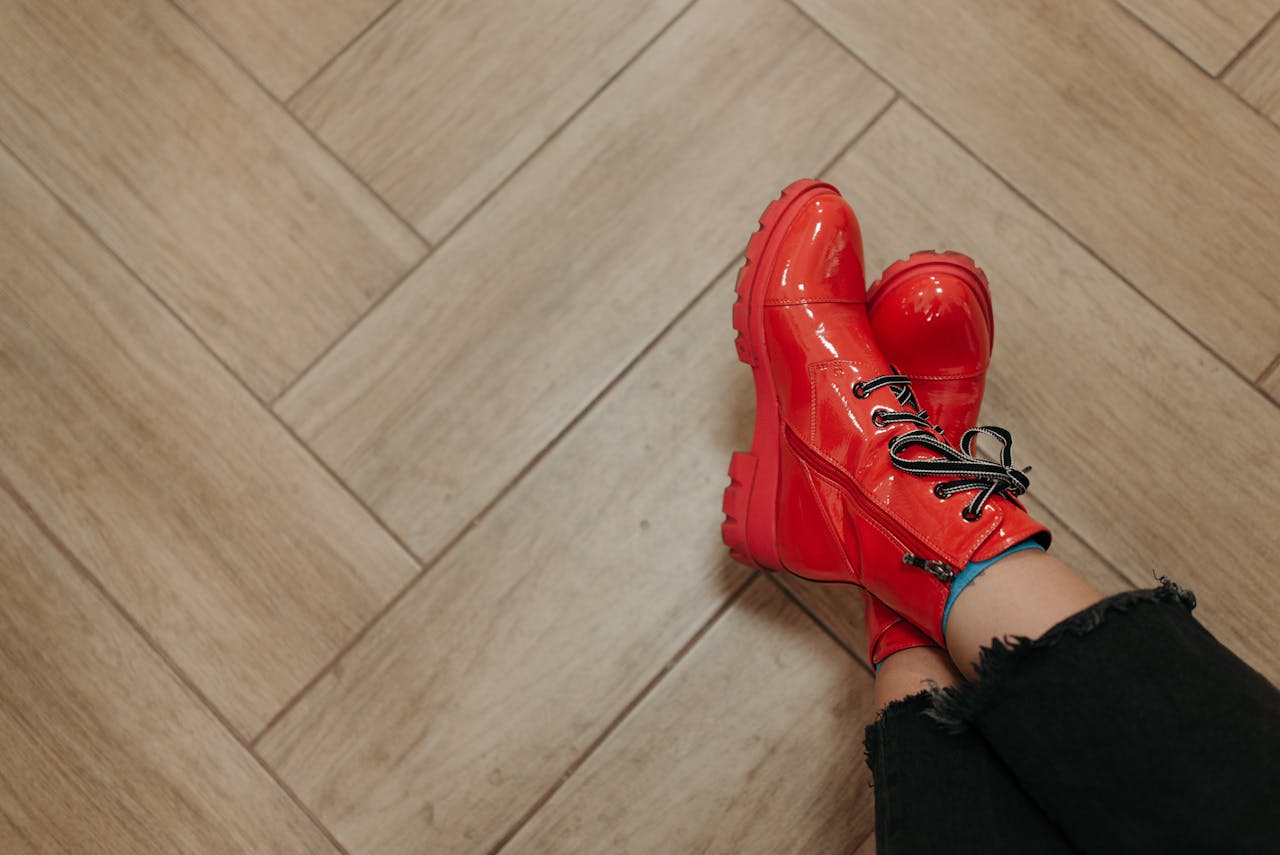 Stylish red boots on a wooden herringbone floor. Fashionable footwear concept.